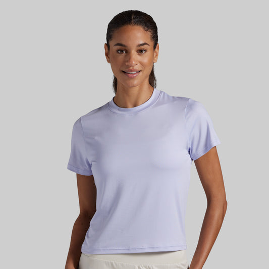 A woman modeling a light lavender short-sleeve crewneck athletic t-shirt against a solid light gray background.