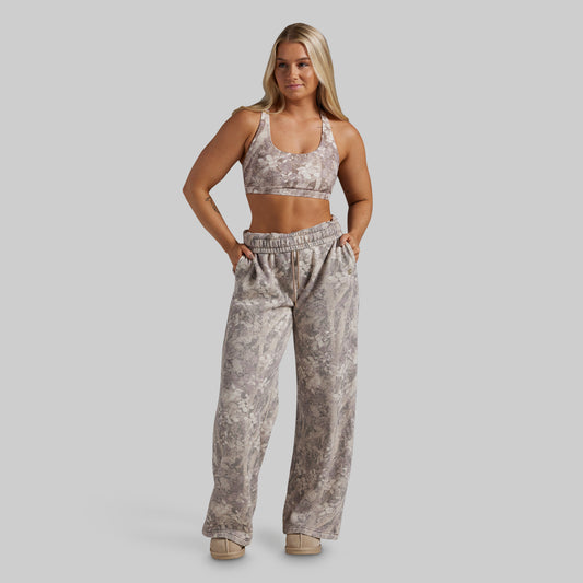 A woman modeling a matching two-piece activewear set featuring a beige and gray camouflage print sports bra and high-waisted, wide-leg sweatpants, set against a solid gray studio background.