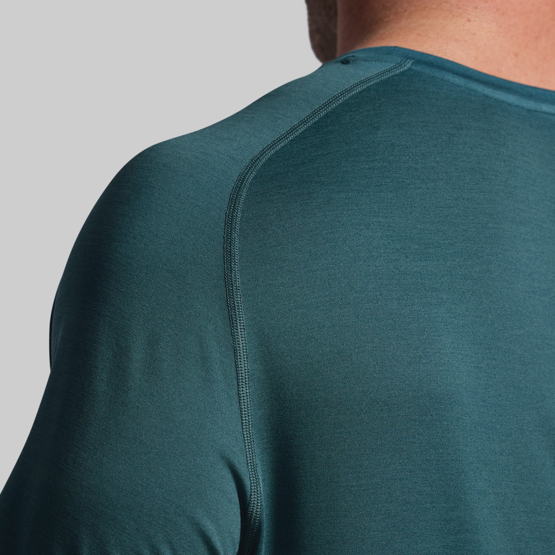 Close-up of a person wearing a teal long-sleeve shirt on a gray background