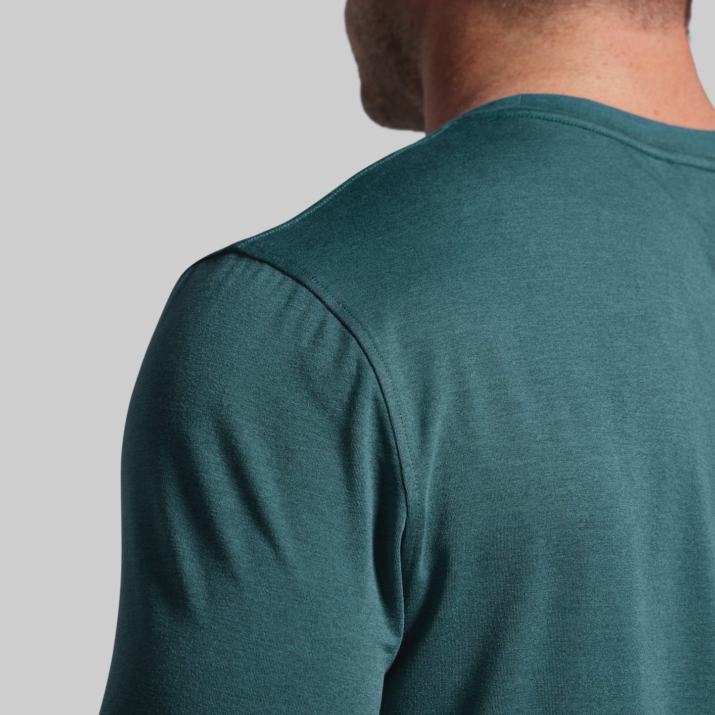 Person wearing a teal long-sleeve shirt on a gray background