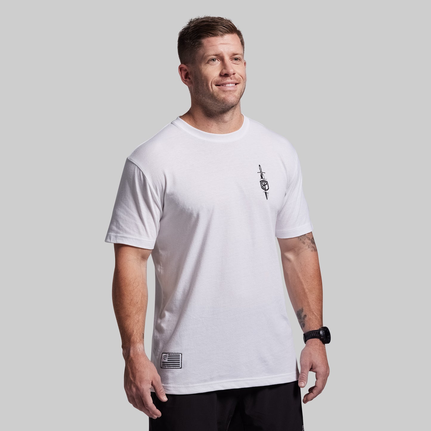 Man wearing a white t-shirt with a small logo on a gray background