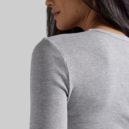 Close-up back view of a woman wearing a light heather gray ribbed long-sleeve top against a plain light gray background.