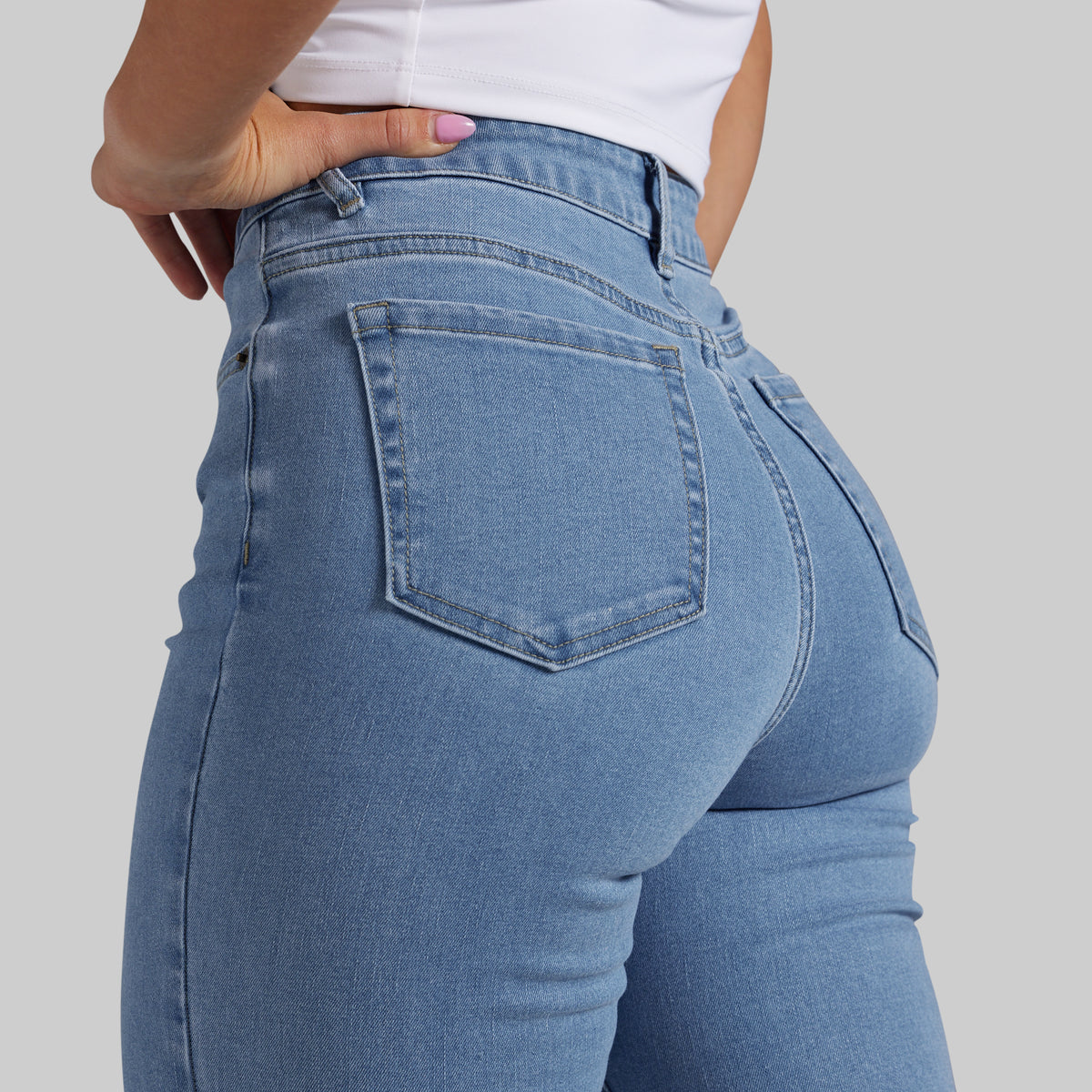 Close-up back view of a person wearing light blue denim jeans with a white top, shown against a plain light gray studio background.