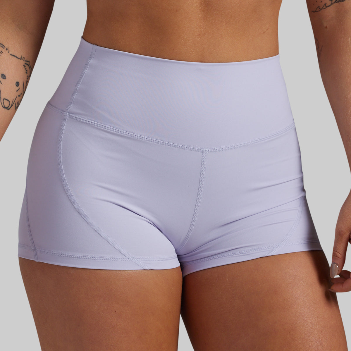 Close-up of a model wearing high-waisted athletic shorts in a light lavender purple color, showing the waistband and hip contours against a solid gray background.