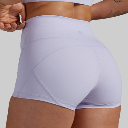 Close-up back view of a model wearing high-waisted light lavender athletic shorts with seam detailing, set against a solid gray background.