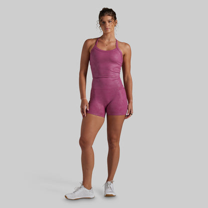 A woman modeling a magenta-pink color athletic set, paired with white sneakers, against a solid light gray background.