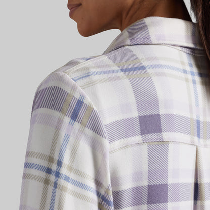 Close-up of a person wearing a white plaid button-up shirt with lavender and blue stripes, showing the collar, shoulder, and side profile against a light gray background.