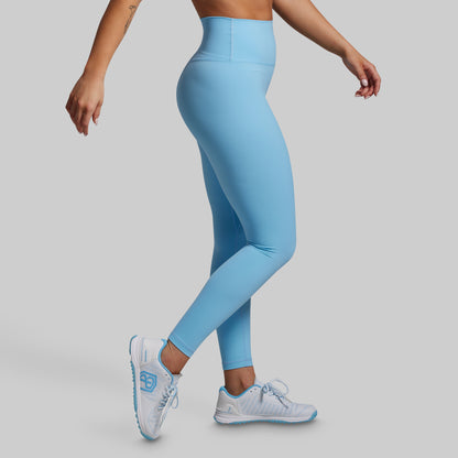 Person wearing light blue leggings and white sneakers on a gray background