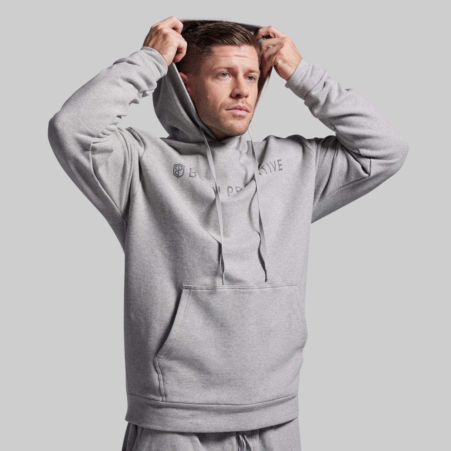 Man wearing a gray hoodie with branding on a light gray background
