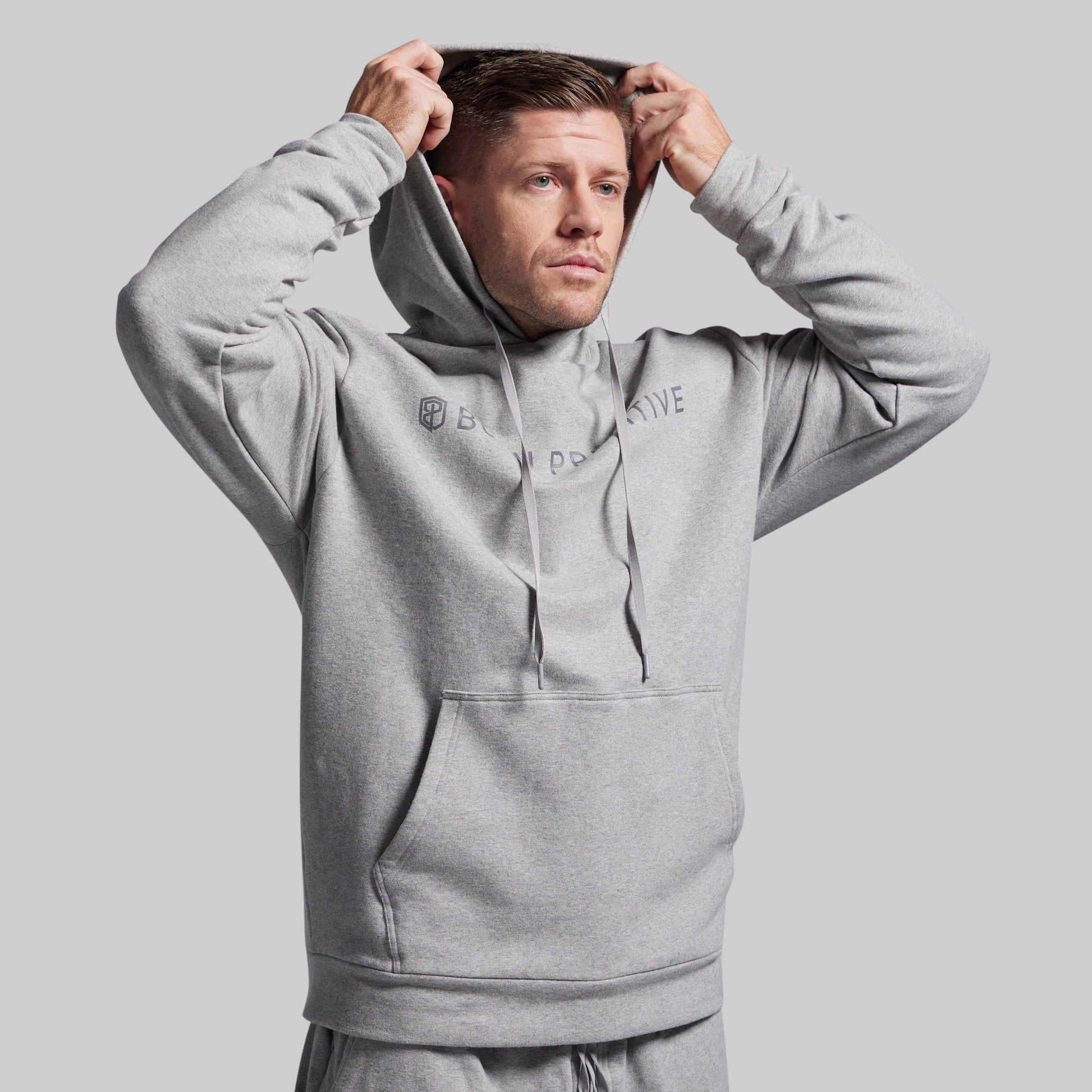 Man wearing a gray hoodie with branding on a light gray background