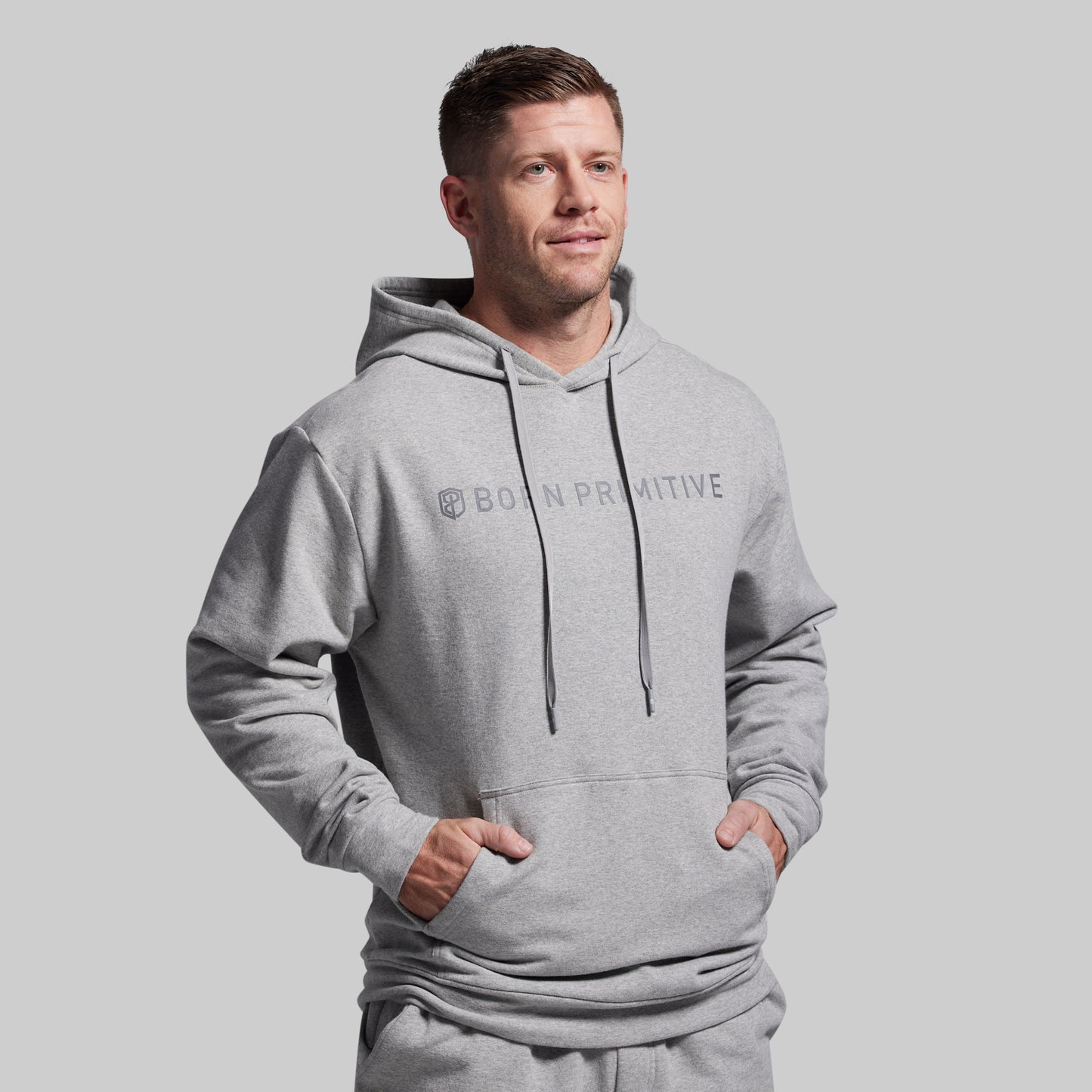 Man wearing a gray hoodie with 'Born Primitive' logo on a light gray background