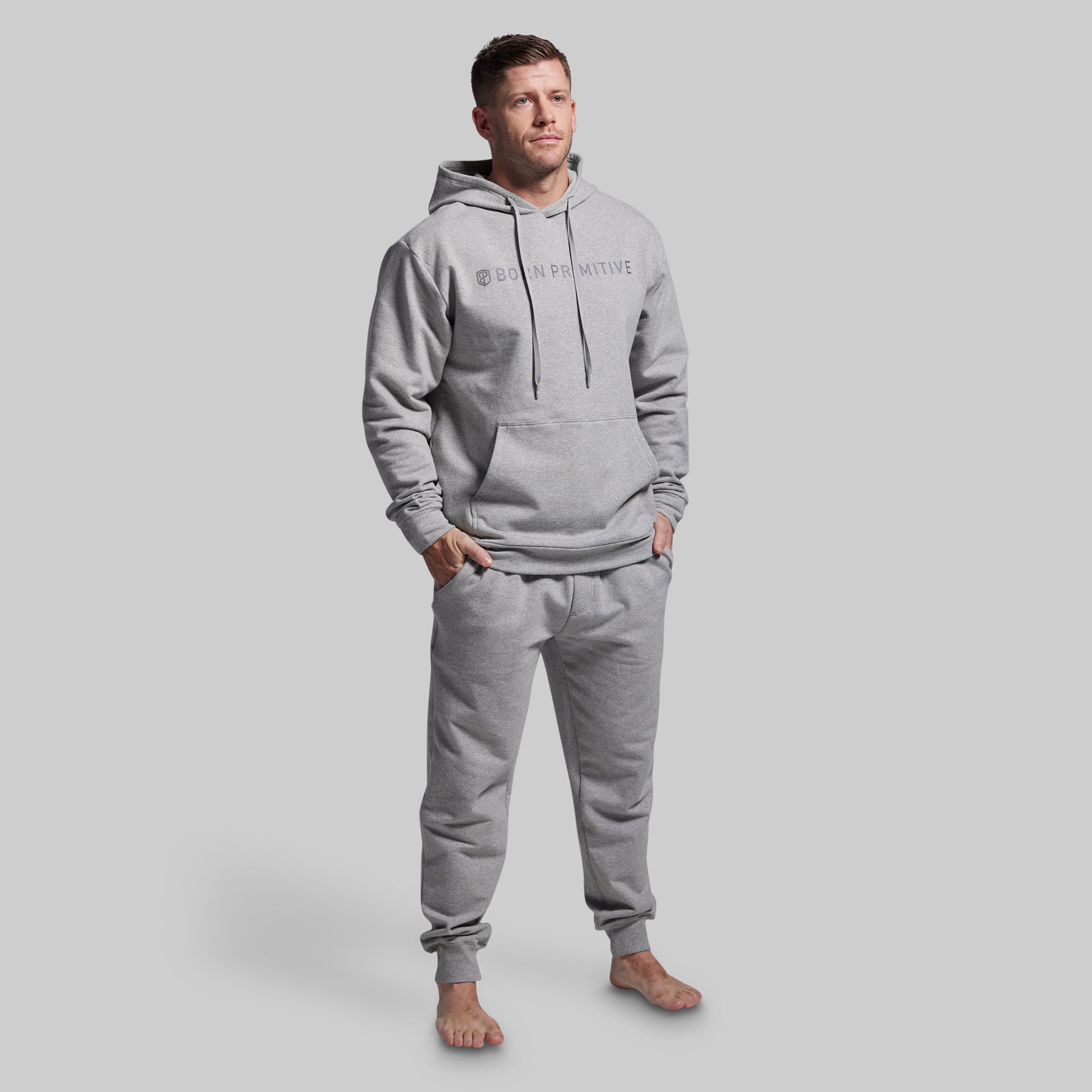 Man wearing a gray hoodie and jogger set with a brand logo on a light gray background