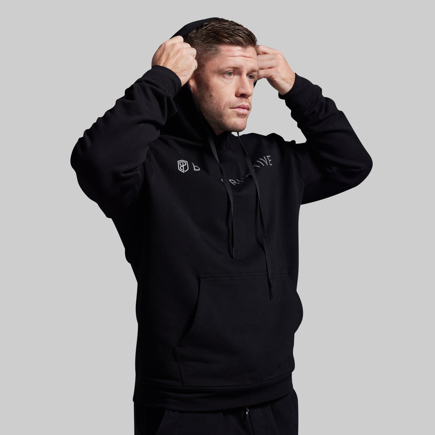 Man wearing a black hoodie with branding on a gray background