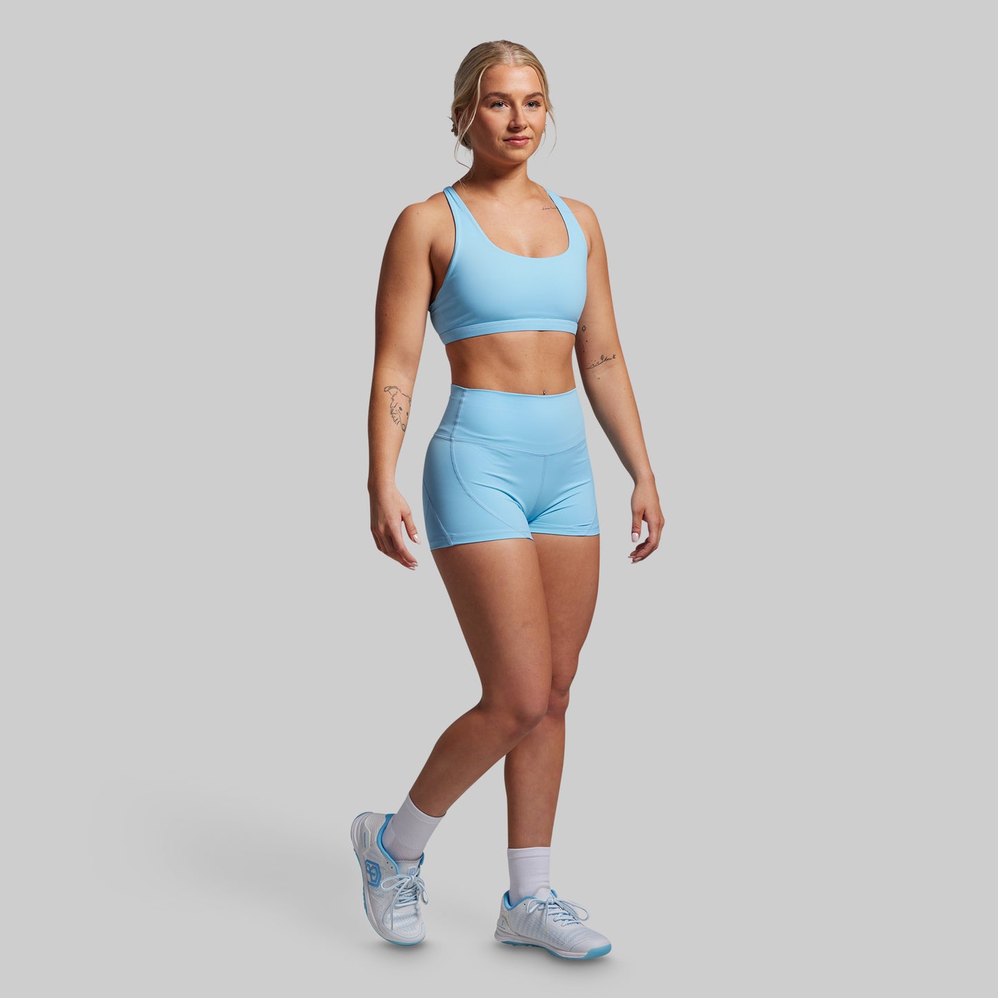Woman wearing a light blue sports bra and shorts set on a gray background