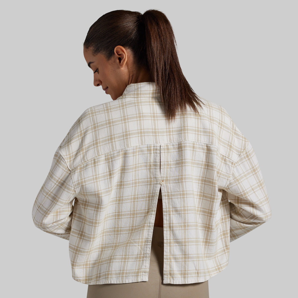 A woman shown from the back wearing a cropped, long-sleeve plaid shirt in beige and white, with a small center back slit.