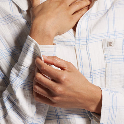 Close-up of a person wearing a light blue and white checkered shirt with hands adjusting the collar.