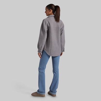 A woman shown from the back wearing a heather gray button-up jacket and light blue jeans, standing against a solid light gray studio background.
