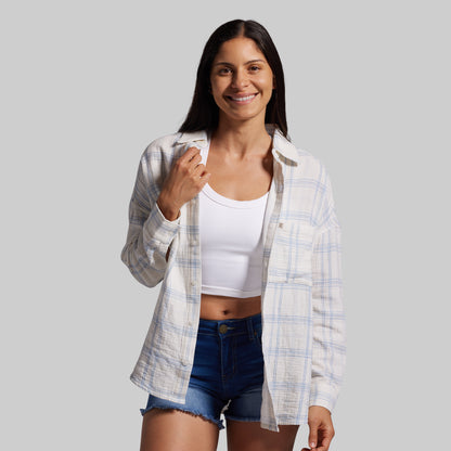 Woman wearing a plaid shirt over a white crop top and denim shorts on a gray background