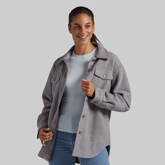A woman wearing a heather gray button-up jacket over a light blue top and blue jeans, standing against a solid gray studio background.