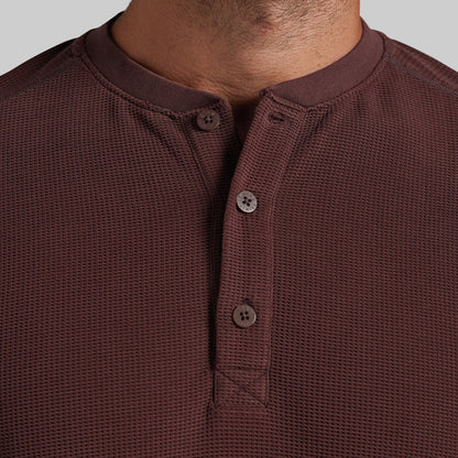 Close-up of a man wearing a textured henley shirt in a deep burgundy brown color, showing the collar, three buttons, and the waffle-knit fabric.