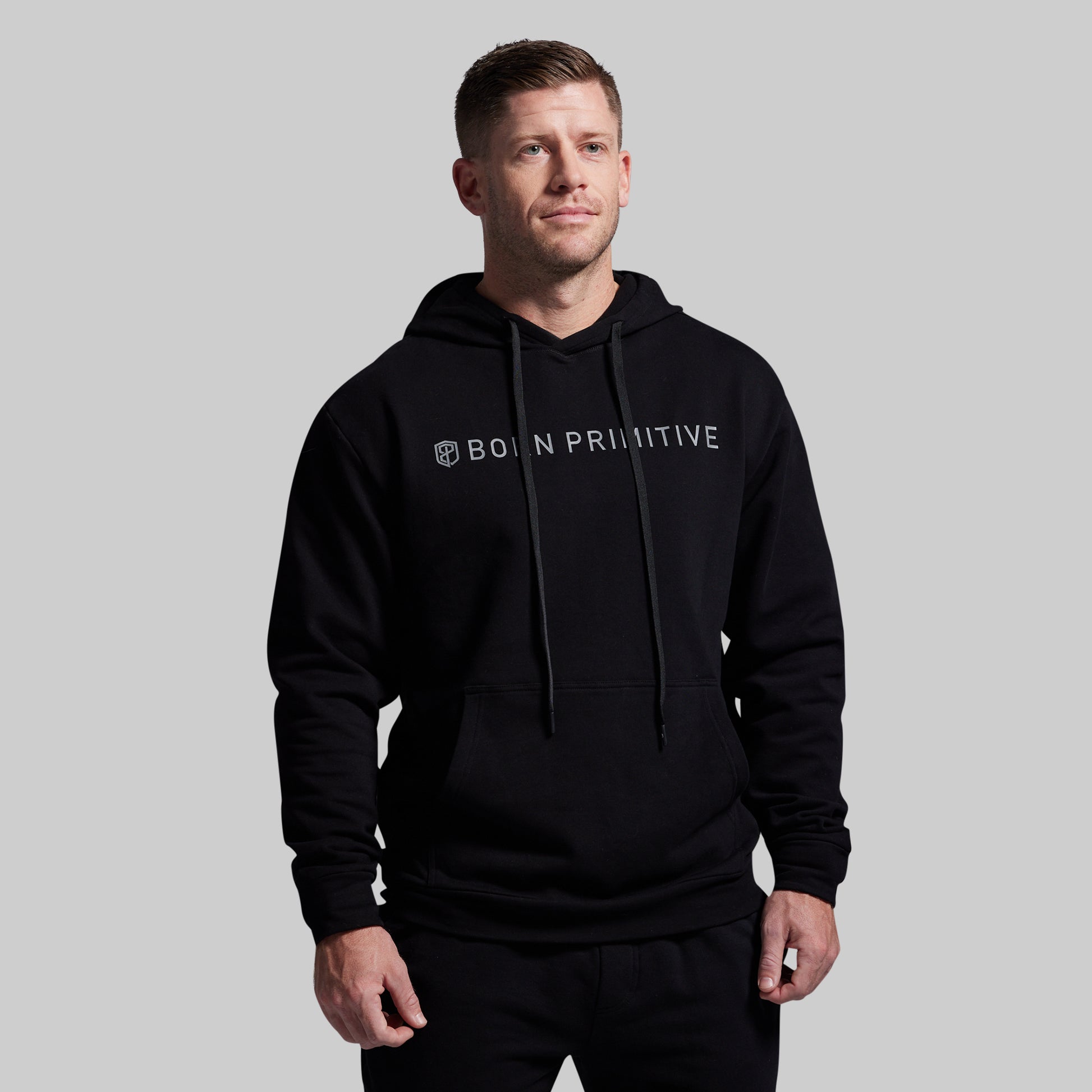 Man wearing a black hoodie with 'BORN PRIMITIVE' logo on a gray background