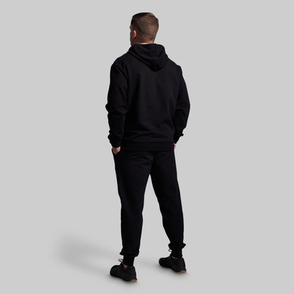 Person wearing a black hoodie and pants on a light gray background
