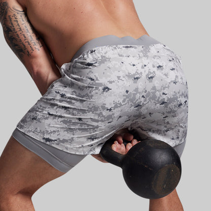 Person wearing camouflage shorts holding a black kettlebell on a plain background