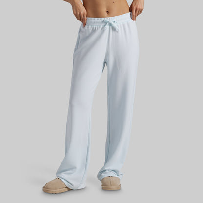 A person wearing light blue wide-leg lounge pants with a drawstring waistband and beige slippers, shown from the waist down against a plain light gray studio background.