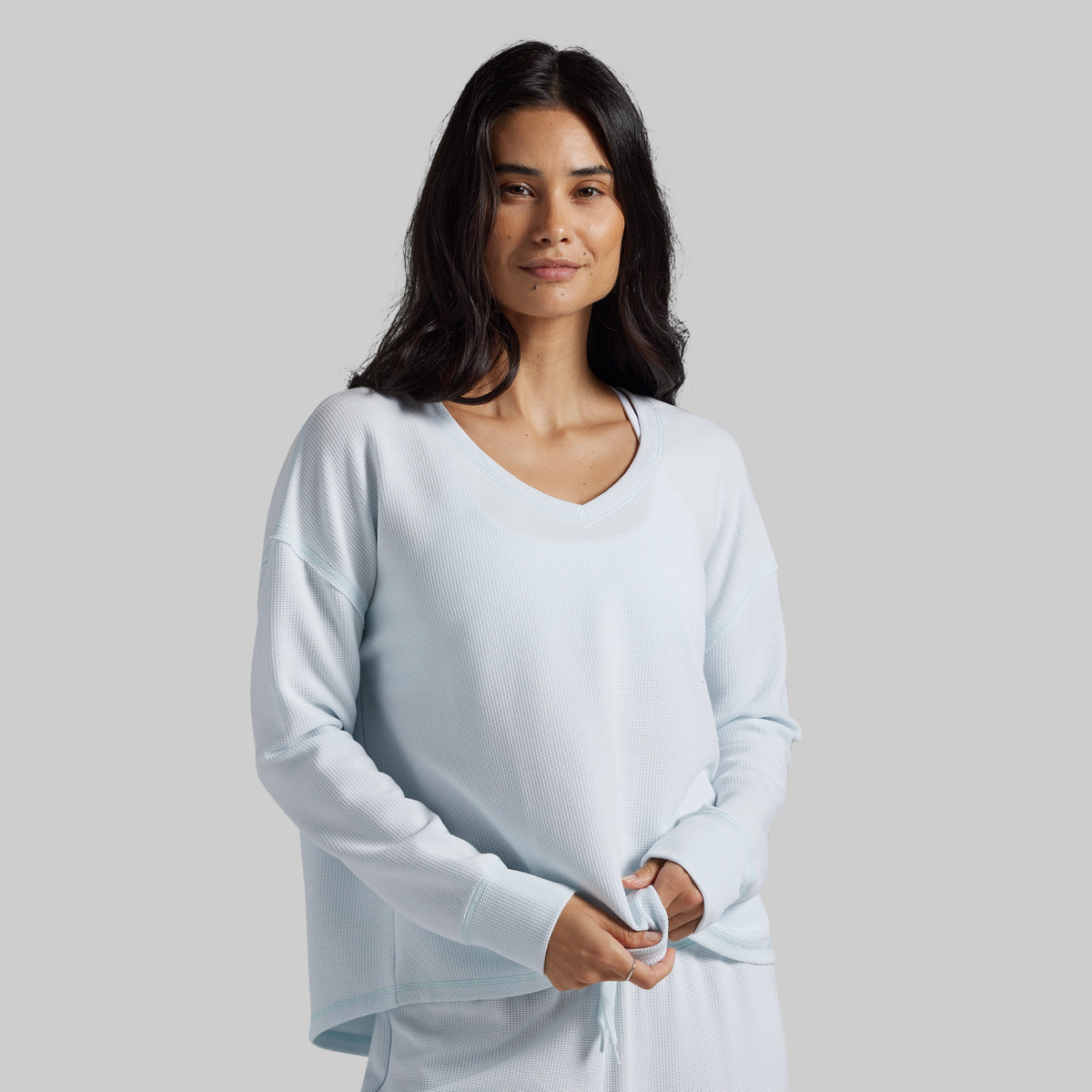A woman modeling a light blue long-sleeve V-neck top against a solid light gray background.