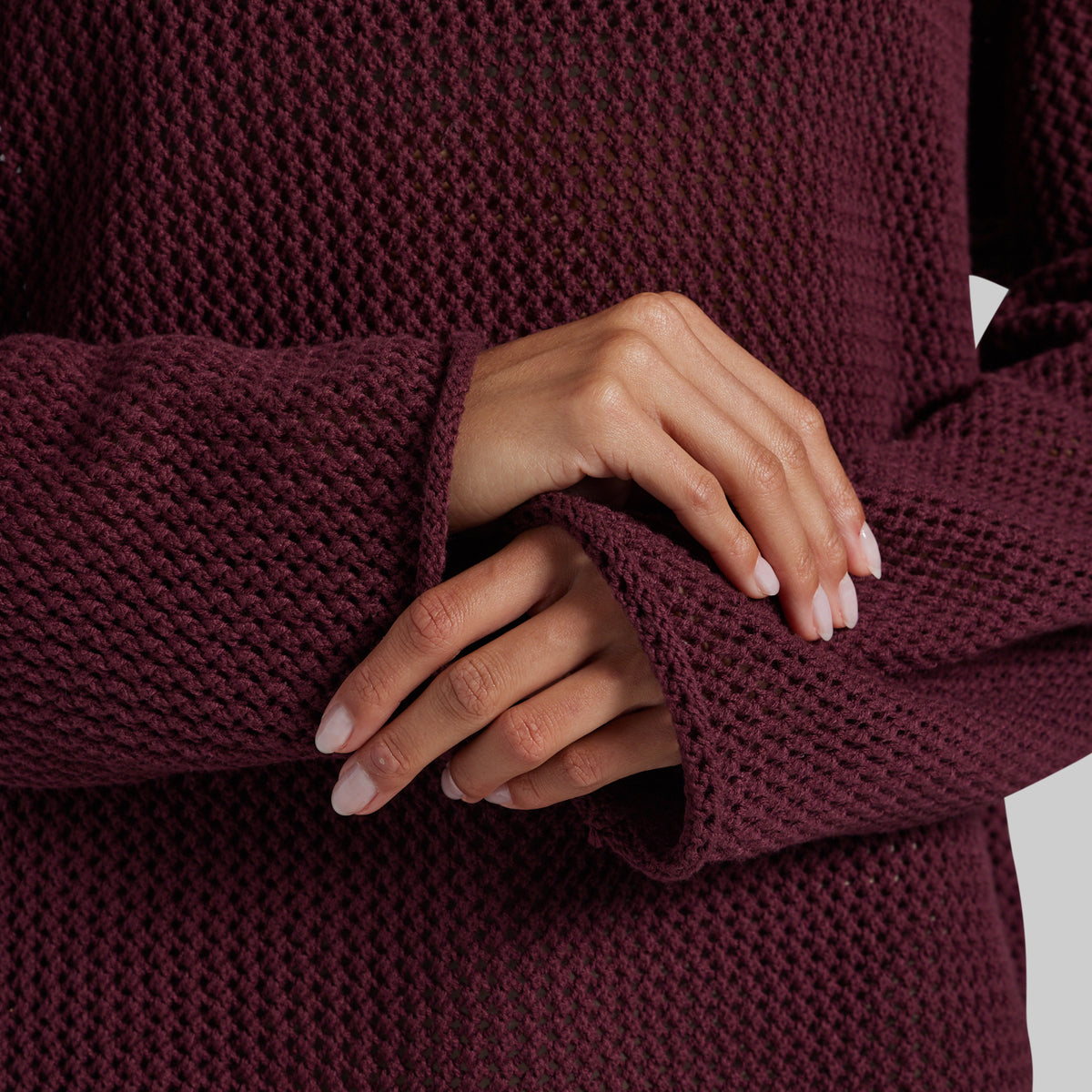 Close-up of a person wearing a chunky knit burgundy sweater, showing the textured fabric and hands resting on the sleeve.