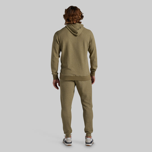 A man viewed from behind wearing a matching olive green hoodie and jogger sweatpants set, standing against a solid light gray background.