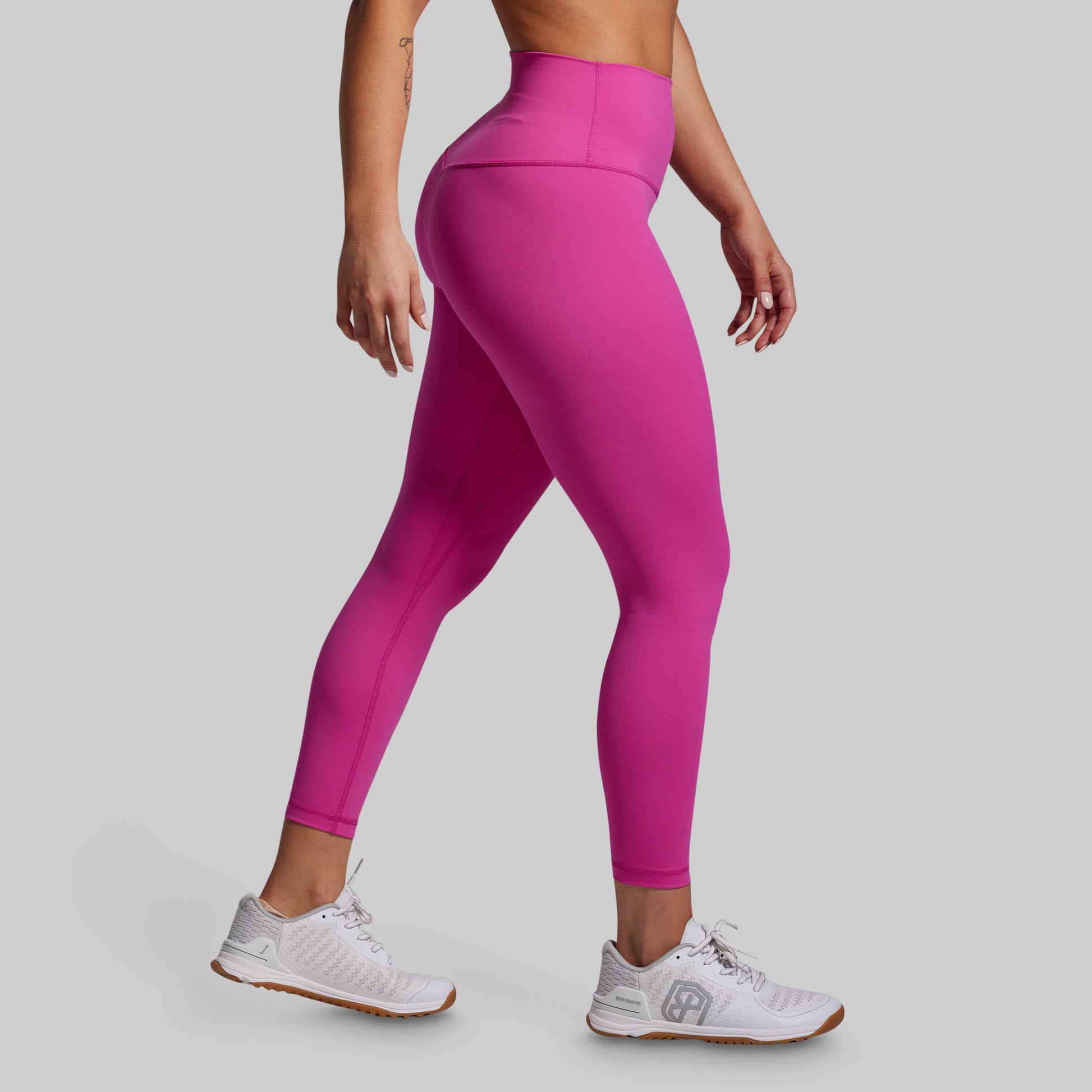Person wearing bright pink leggings and white sneakers on a gray background