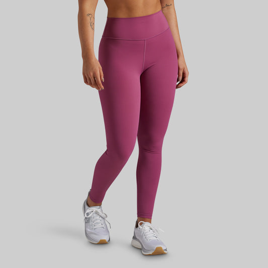 A model wearing high-waisted, form-fitting leggings in a dusty rose or mauve shade, paired with white athletic sneakers, shown from the waist down against a solid light gray background.