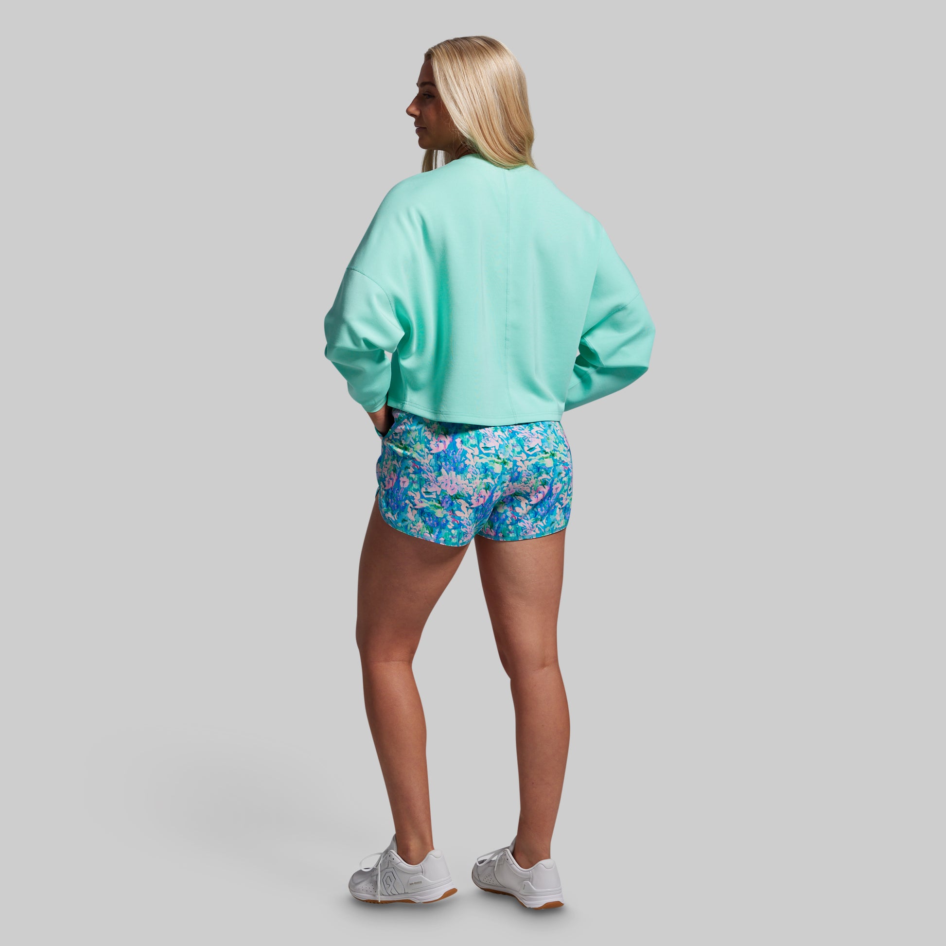 Person wearing a light blue sweatshirt and floral shorts on a gray background