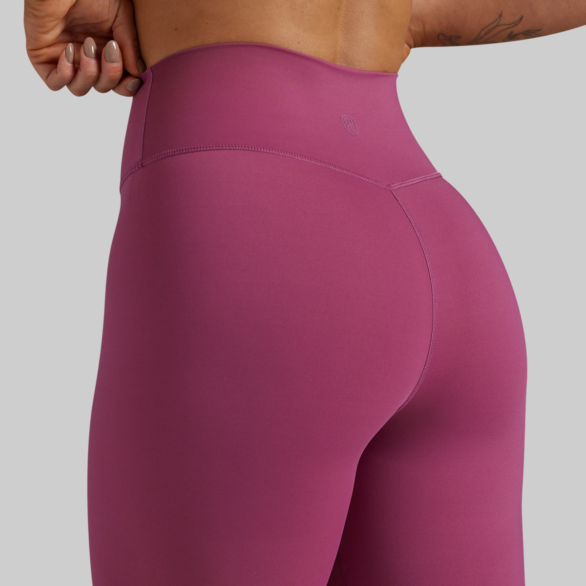 Close-up back view of a person wearing high-waisted athletic leggings in a muted berry pink color, showing the waistband and hip area against a plain light gray background.