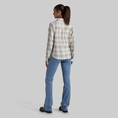 A woman shown from the back wearing a beige and white plaid button-down shirt and light blue jeans, standing against a solid gray studio background.