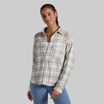 A woman modeling a long-sleeve plaid button-up shirt in beige, white, and light brown tones, paired with blue jeans, against a solid gray background.