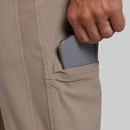 Close-up of a person's hand pulling a silver smartphone out of a side pocket of light beige trousers against a light gray background.