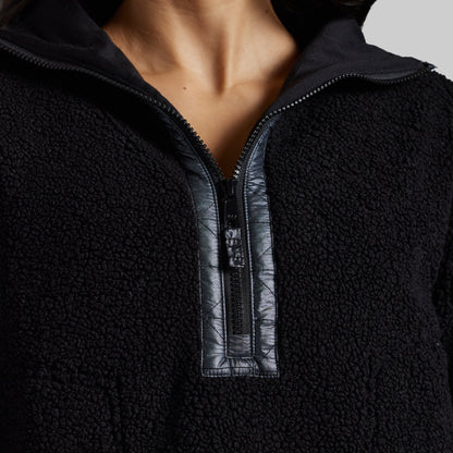 Close-up of a person wearing a black sherpa fleece quarter-zip pullover with a contrasting black faux-leather placket and zipper trim.