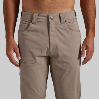 A close-up of a person wearing khaki cargo pants, showing the front waistband, belt loops, button, front pockets, and side cargo pocket against a plain light gray background.