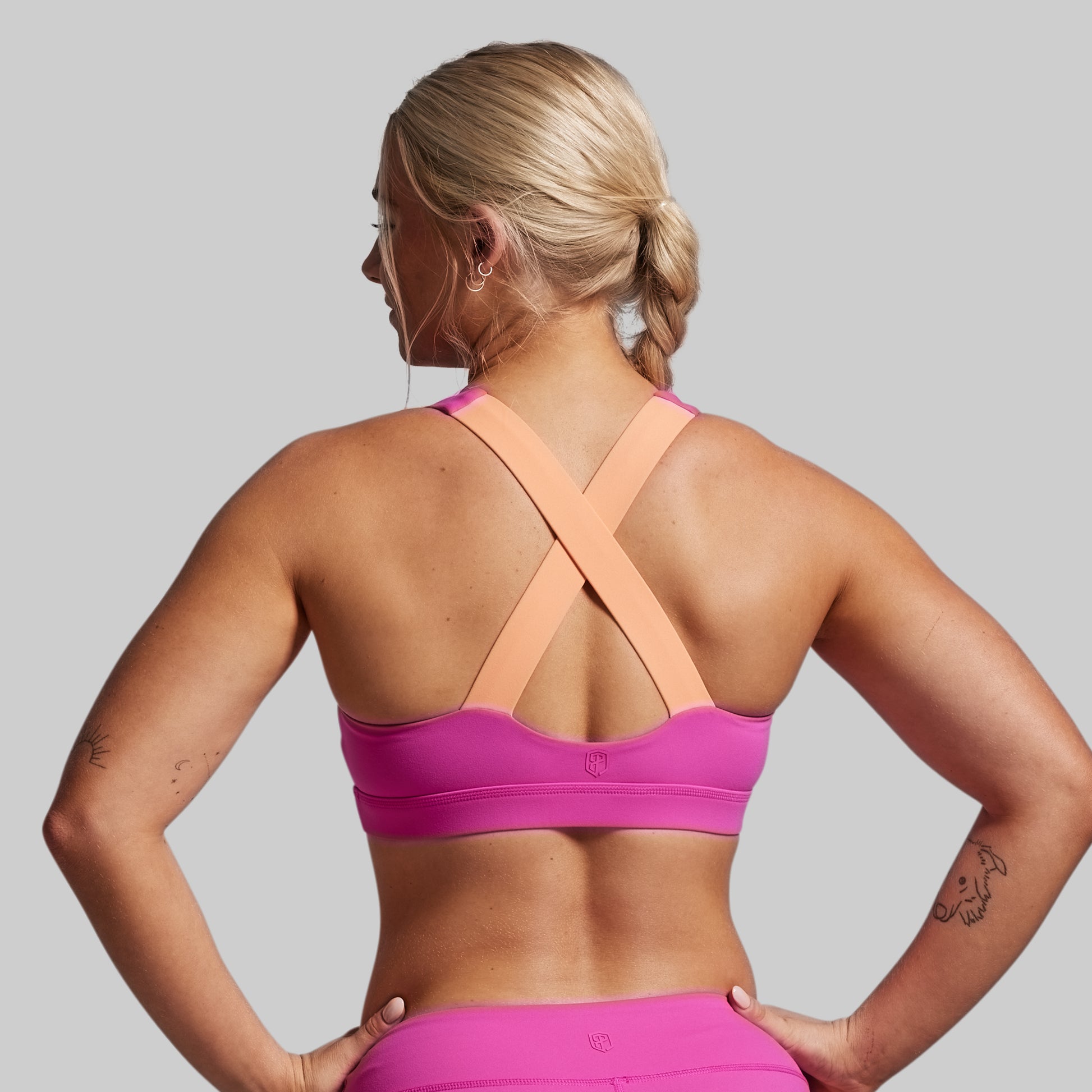 Woman wearing a pink sports bra and leggings on a gray background