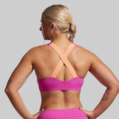Woman wearing a pink sports bra and leggings on a gray background