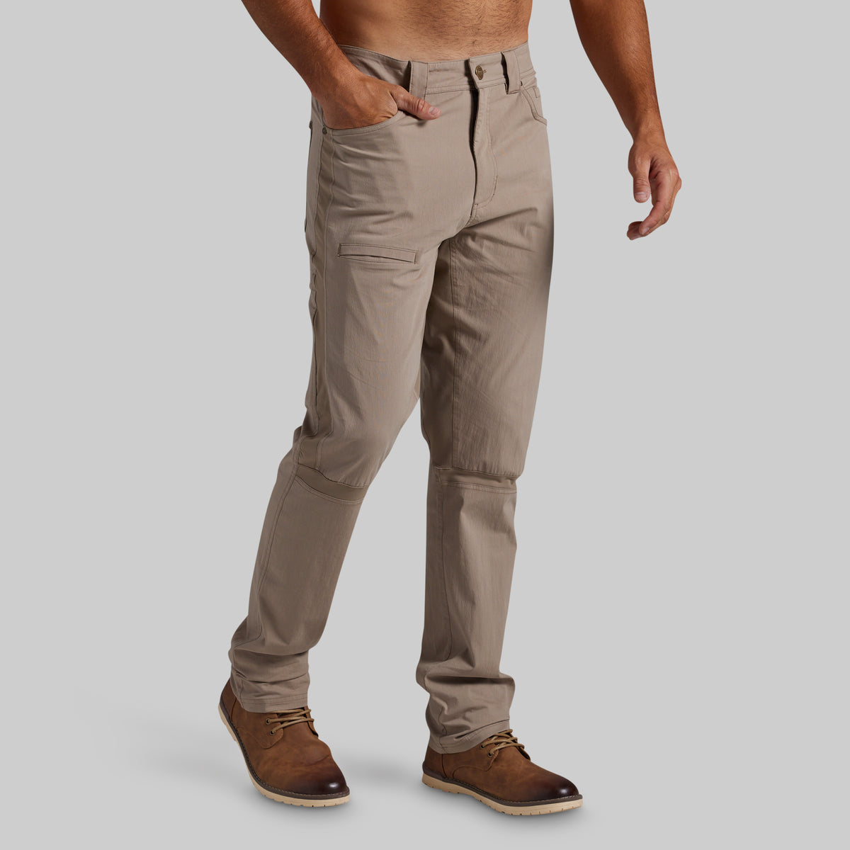 A man wearing beige cargo-style pants and brown leather shoes, shown from the waist down against a plain light gray studio background.