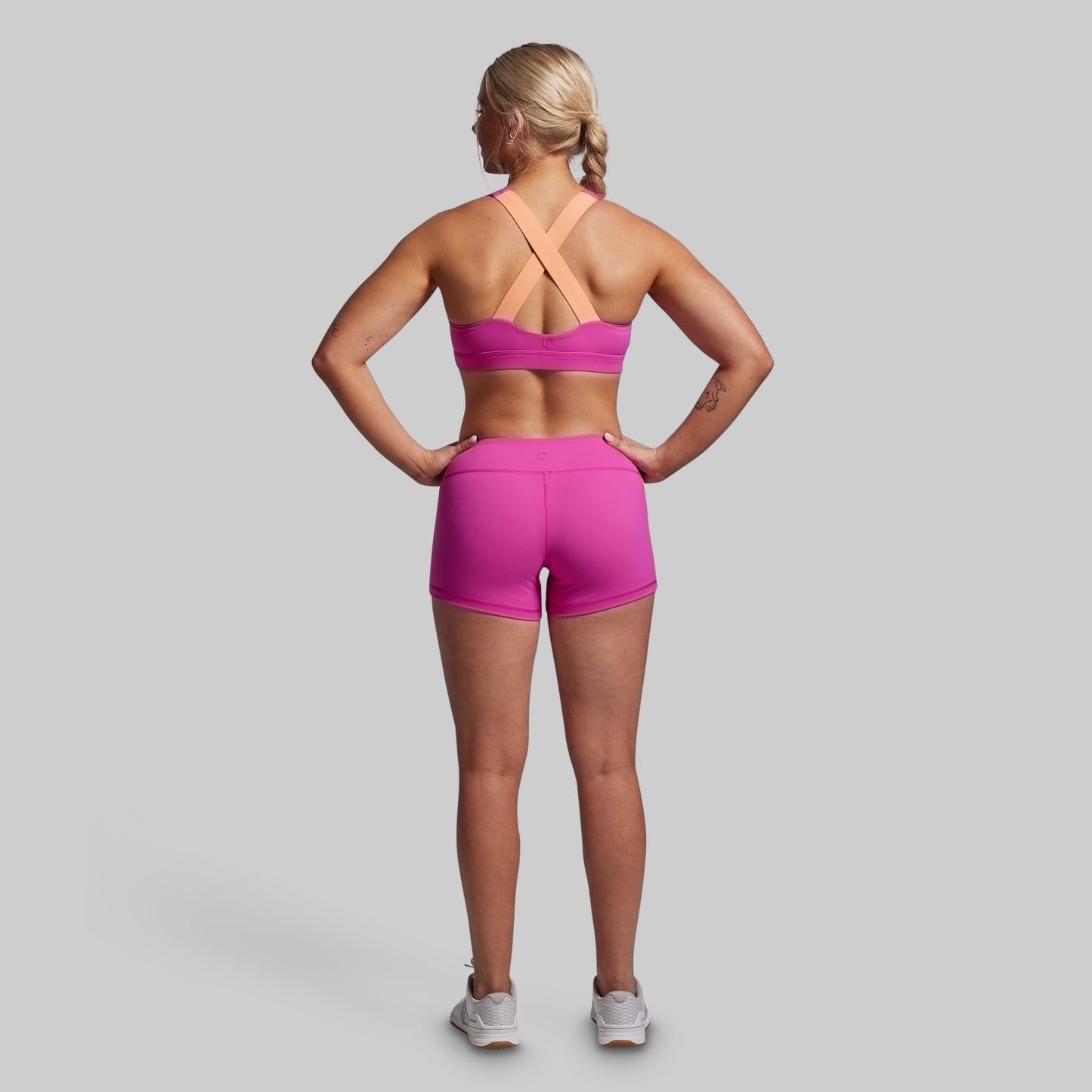 Woman wearing a pink sports bra and shorts on a gray background