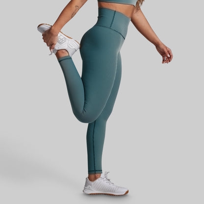 Person wearing teal leggings and white sneakers on a plain background