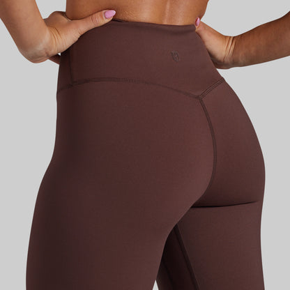 Close-up of a model wearing high-waisted brown activewear yoga pants, showing the waistband, hip seam, and back side against a solid gray background.