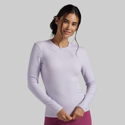A woman modeling a light lavender long-sleeve athletic top against a solid gray studio background.