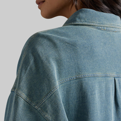 Close-up of a person wearing an oversized blue denim shirt, showing the back collar, shoulder, and denim texture against a light gray background.