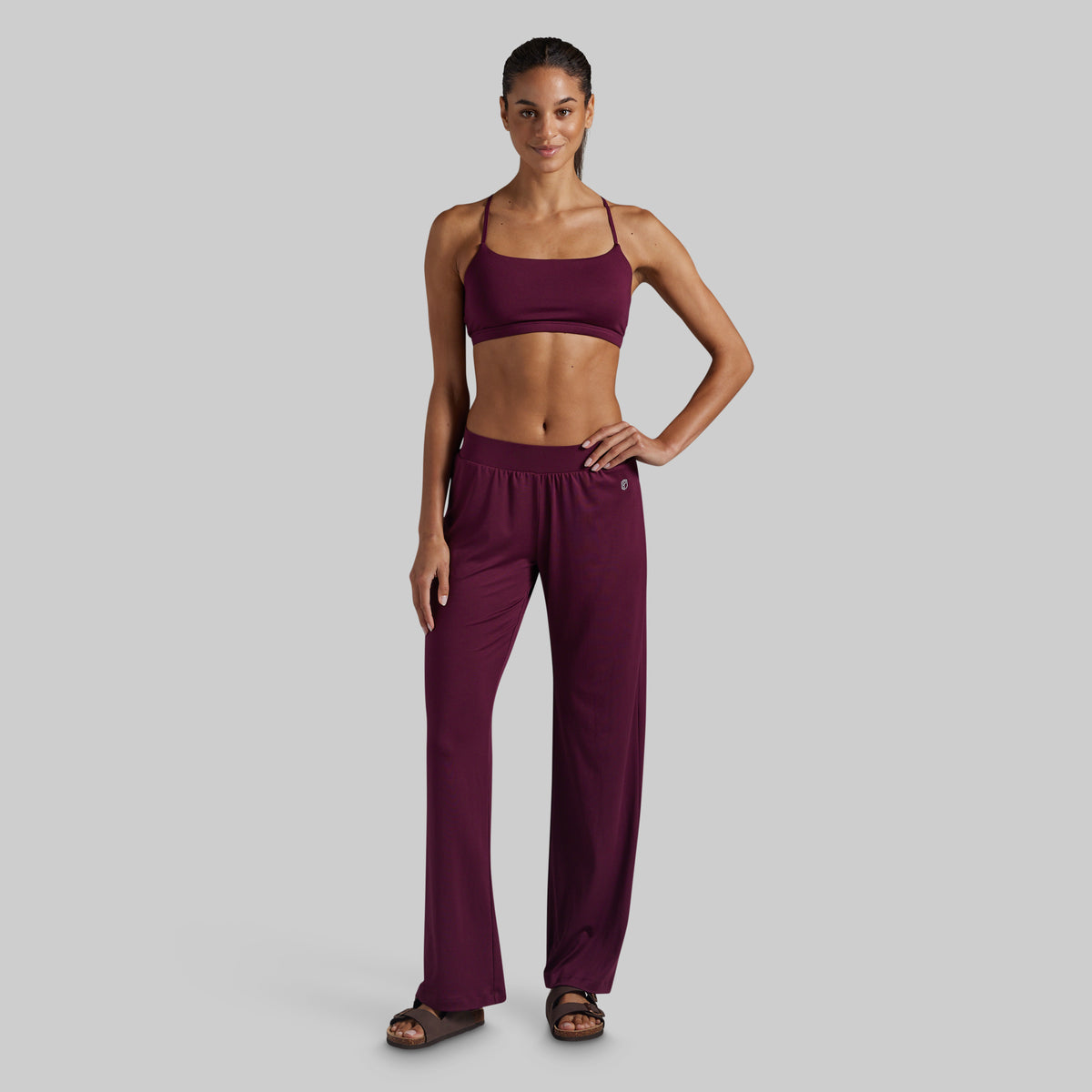 A woman modeling a matching two-piece loungewear set in deep burgundy, featuring a spaghetti-strap lounge bra and high-waisted wide-leg pants.