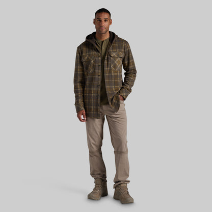 A man modeling a brown and olive green plaid hooded flannel shirt jacket, styled with a dark olive t-shirt, beige cargo pants, and brown boots, against a solid gray background.